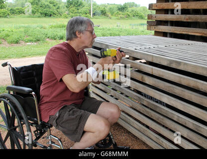 Disabled man in a wheelchair doing carpenter repair work with a cordless drill Stock Photo