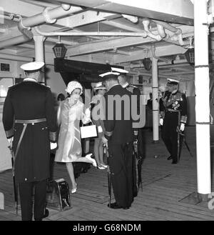 Queen Elizabeth II shows her shoe to high-ranking officers aboard HMS Eagle. The officers were inspecting the show to make sure the heel remained intact after she had negotiated a ship's ladder during herb visit to the aircraft carrier in Torbay, Devon. Stock Photo