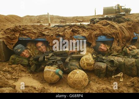 Members of 40 Commando Royal Marines dug in north of the Al Faw Peninsula, aproaching Basra, after heavy rainstorms in the desert, Marine Omar Rawlings, 20, (left) Marine Delme King, 24, and Jim Morton shelter in their fox hole. Stock Photo