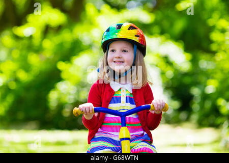 Cute girl wearing safety helmet riding her tricycle in sunny summer park. Kids ride bicycle. First bike for little child Stock Photo