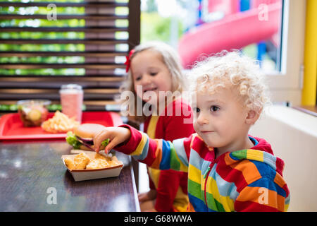 Little girl and boy eating chicken nuggets, hamburger and French fries in a fast food restaurant. Child with sandwich Stock Photo