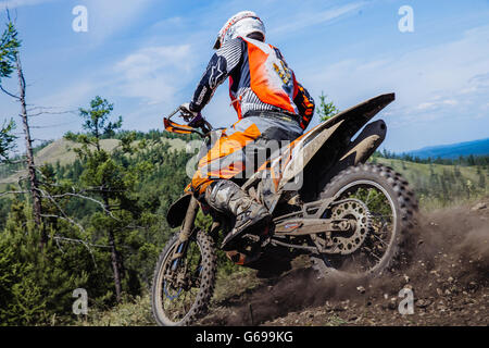 rider going down a hill, dirt and stones from under wheels during Ural Cup in Enduro Stock Photo