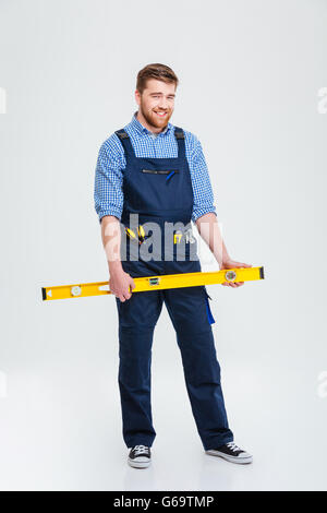 Full length portrait of a smiling male builder holding waterpas isolated on a white background Stock Photo