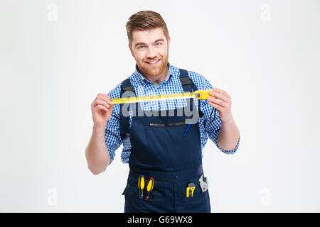 Cheerful attractive young worker in overall smiling and holding measuring tape Stock Photo