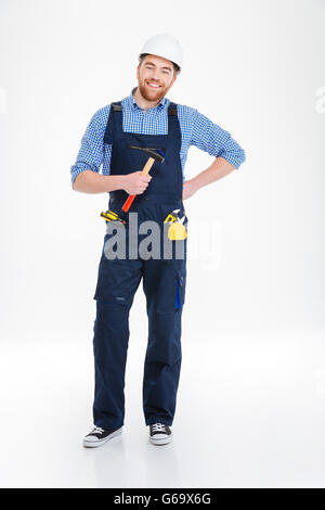 Happy young builder in helmet standing and holding hammer Stock Photo