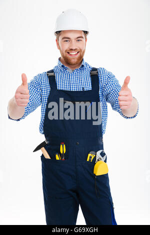 Happy attractive young builser in helmet showing thumbs up with both hands Stock Photo