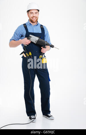 Cheerful handsome young builder in helmet standing and holding drill Stock Photo