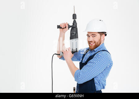 Cheerful handsome young worker in helmet using drill and pointing up Stock Photo