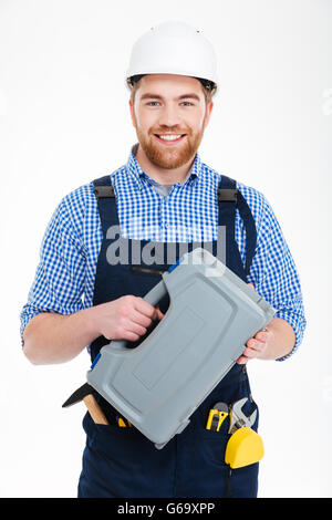 Smiling bearded young worker in helmet holding tool box Stock Photo