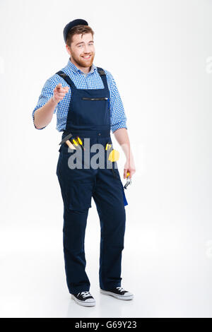 Smiling bearded young man builder in overall and cap pointing on you Stock Photo