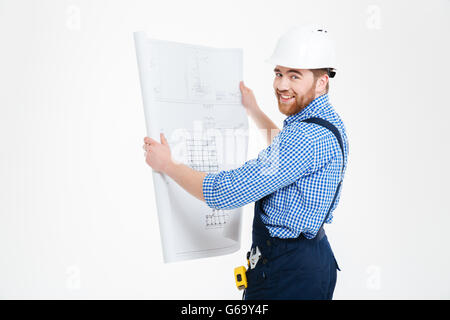 Cheerful attractive builder in helmet working with blueprint and smiling Stock Photo