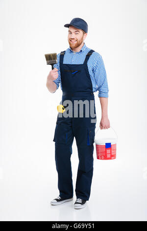 Happy bearded young man painter with can paint and brush standing and smiling Stock Photo