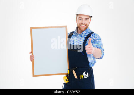Cheerful attractive young builder holding blank whiteboard and showing thumbs up Stock Photo
