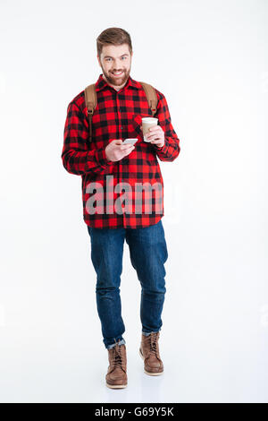 Full length portrait of a smiling man drinking coffee and using smartphone isolated on a white background Stock Photo