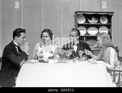 1930s TWO COUPLES FOUR MEN AND WOMEN SEATED AT DINING TABLE WEARING FORMAL CLOTHES Stock Photo
