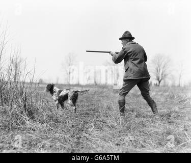1920s MAN HUNTER WITH SHOTGUN IN FIELD WITH ENGLISH SETTER HUNTING DOG ON POINT Stock Photo