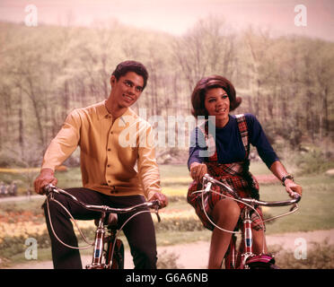 1960s AFRICAN AMERICAN TEENAGE BOY AND GIRL RIDING BICYCLES Stock Photo