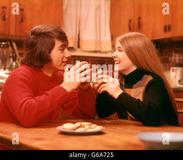 1970 1970s YOUNG TEENAGE TEEN COUPLE EAT COOKIE COOKIES DRINK BOY GIRL BOYS GIRLS DATE DATING FRIEND FRIENDS KITCHEN TABLE Stock Photo