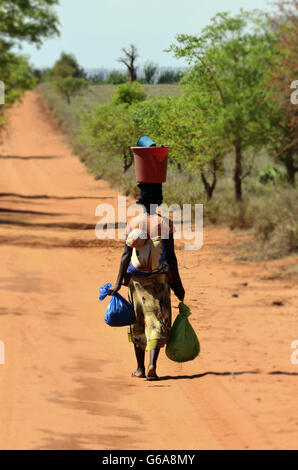 Antandroy, Malagasy woman,carrying a baby on the back water bucket on the head and bags on both hand Stock Photo