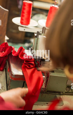 Red cloth being ruffled through a sewing machine by seamstress Stock Photo