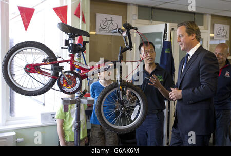 Prime Minister David Cameron, right, looks at a bike that is being reconditioned as he speaks to technician Ken Tang, during a visit to promote cycling in Watford. Stock Photo