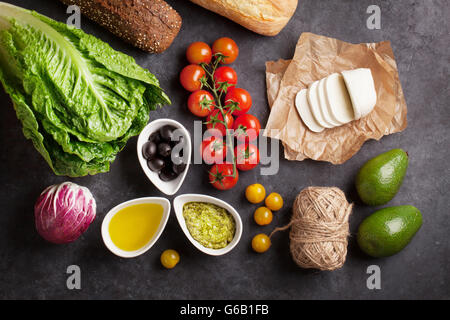 Cooking food ingredients. Lettuce salad, avocado, olives, cheese, bread and tomato cherry over stone background. Top view Stock Photo