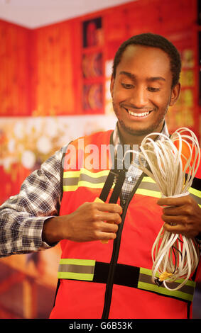 Young electrical worker wearing safety vest, holding cables and cable pliars, smiling with great positive attitude Stock Photo