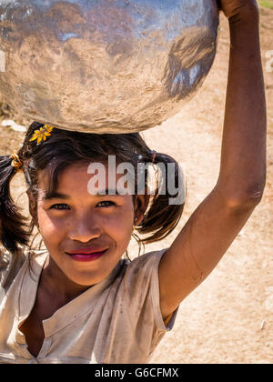 Young woman carrying water in an aluminum jug on her head. Stock Photo