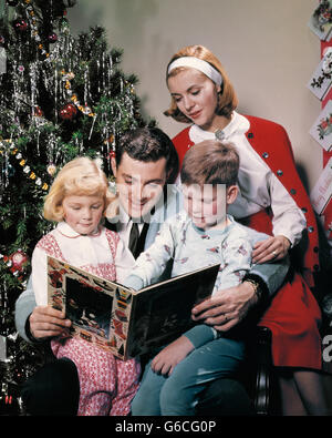 1960s FAMILY BY CHRISTMAS TREE FATHER READING BOOK THE NIGHT BEFORE CHRISTMAS TO SON DAUGHTER WIFE Stock Photo