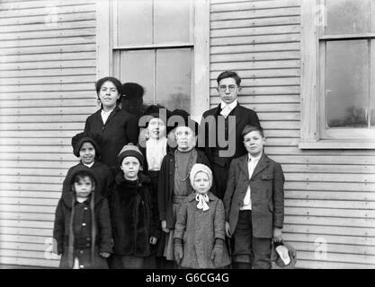1900s GROUP PORTRAIT CHILDREN BOYS GIRLS STANDING POSING BY HOUSE Stock Photo