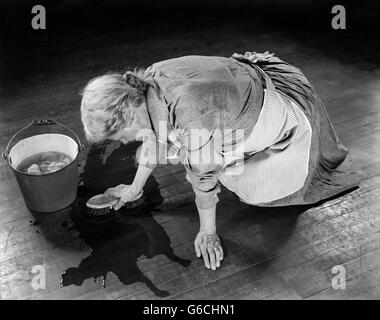 1920s 1930s SENIOR WOMAN WASHING FLOOR ON HER HANDS AND KNEES WITH BUCKET SCRUB BRUSH Stock Photo