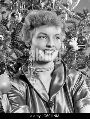 1940s 1950s PORTRAIT SMILING WOMAN WITH CHRISTMAS TREE WEARING SATIN BLOUSE PEARL NECKLACE Stock Photo