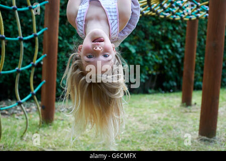 Portrait of Happy little blond girl playing on a rope web playground outdoor, upside down Stock Photo