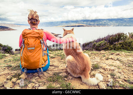 Woman hiker looking at sea with akita inu dog on seaside trail. Recreation and healthy lifestyle outdoors in summer mountains an Stock Photo