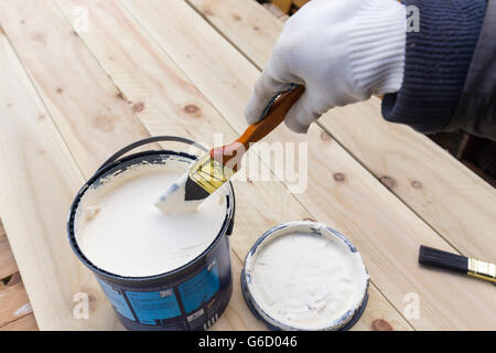 Holding painting brush over the jar with the white paint. Painting timber boards outside with the white paint Stock Photo
