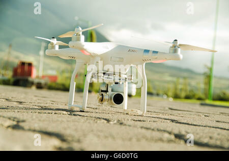 White drone with camera mounted underneath sitting on concrete surface, mountain landscape background Stock Photo