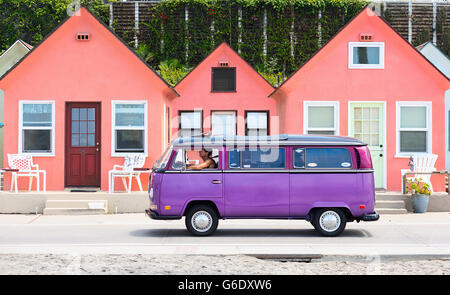 A man drives a purple Volkswagen van down a road in front of a row of pink houses in Oceanside, Calif., on Aug. 3, 2014. Stock Photo