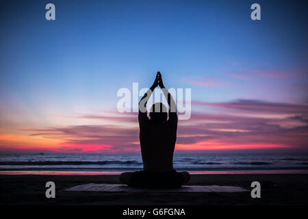 Man silhouette doing yoga exercise at sunset beach Stock Photo