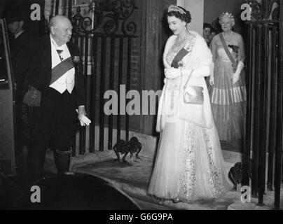 Wearing his sash as Knight of the Garter, Sir WInston Churchill opens the door of Queen Elizabeth's car, as she leaves after dining with him and the Duke of Edinburgh and other distinguished guests. Watching the doorway is her hostess Lady Churchill. Stock Photo