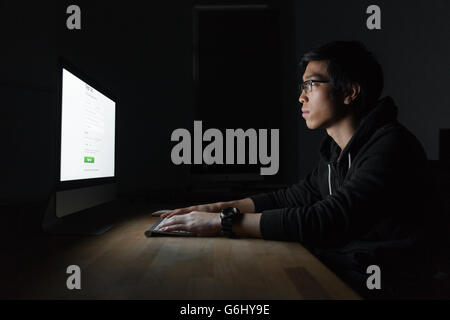 Handsome asian young man sitting and using computer in dark room Stock Photo