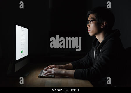 Concentrated asian young man in glasses using computer in the evening in office Stock Photo