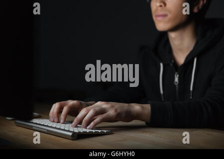 Closeup of serious asian young man sitting and typing on keyboard in dark room Stock Photo