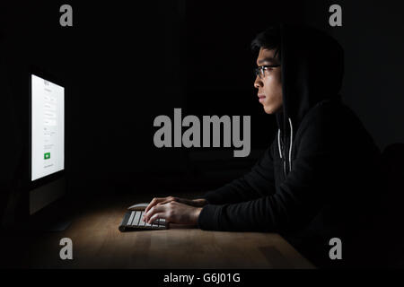 Concentrated young hacker using computer and stealing information in dark room Stock Photo