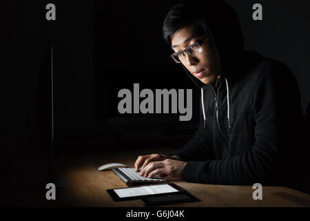 Hacker sitting and using laptop, tablet and smartphone in dark room Stock Photo