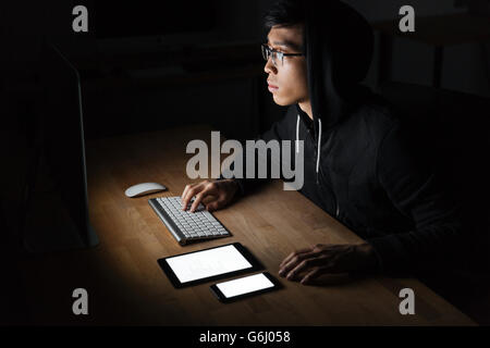 Hooded computer hacker stealing information using blank screen tablet and smartphone Stock Photo