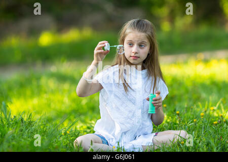 Little girl blowing bubbles sitting on the grass in the Park. Stock Photo