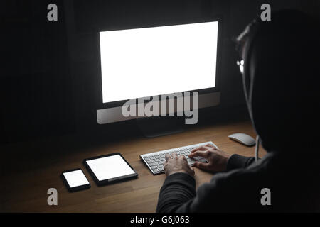 Back view of hacker using blank screen computer, tablet and cell phone in dark room Stock Photo