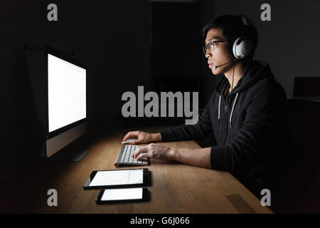 Man in headphones using blank screen computer, tablet and mobile phone in dark room Stock Photo
