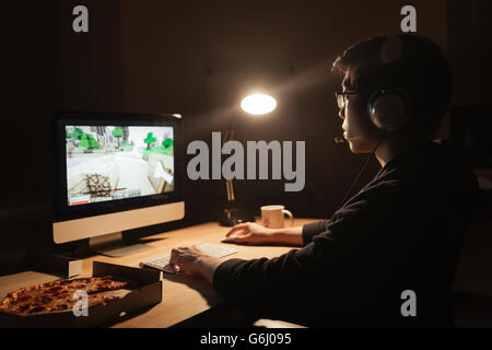 Male gamer playing computer game and eating pizza in dark room Stock Photo