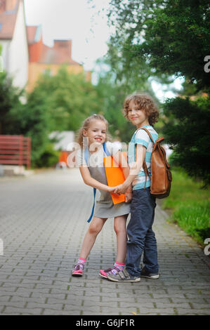 Two pupils of elementary school, boy and girl, on the way to school. Children have a good mood. They hold hands and with a smile Stock Photo